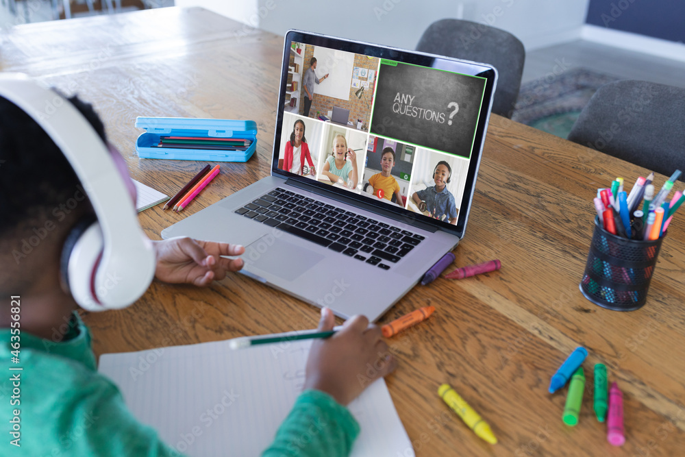 African american boy using laptop for video call, with diverse elementary school pupils on screen