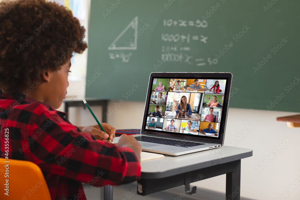 African american boy using laptop for video call, with diverse elementary school pupils on screen