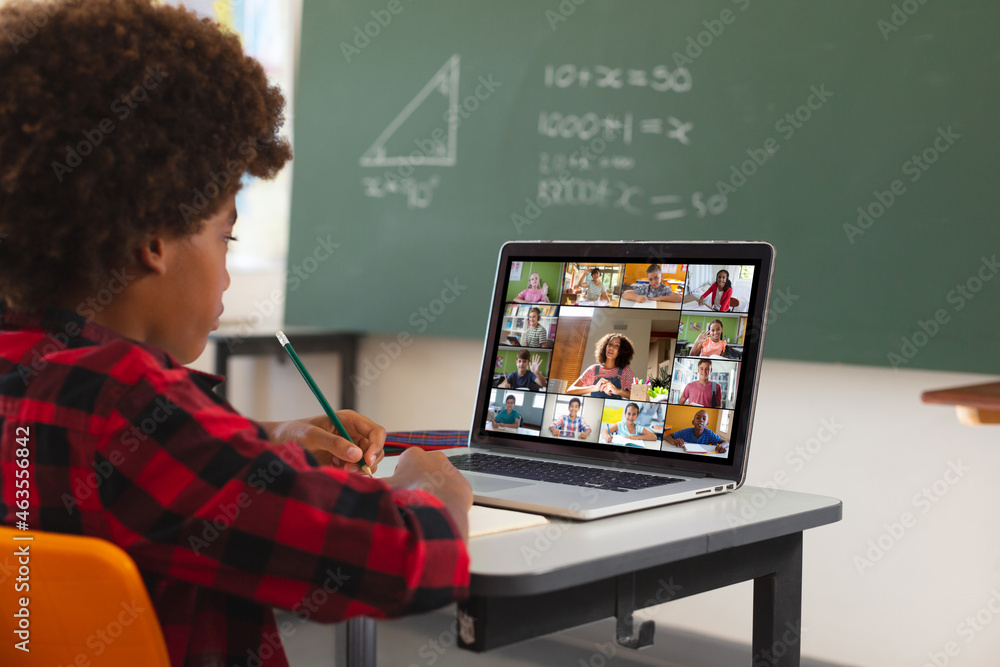 African american boy using laptop for video call, with diverse elementary school pupils on screen