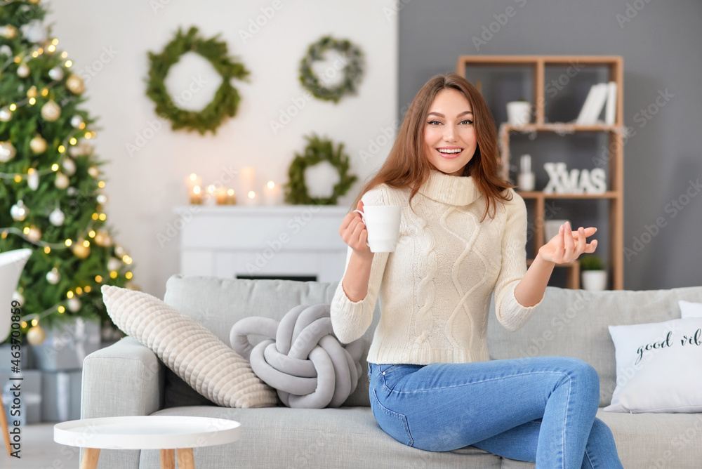 Beautiful young woman with cup of hot cacao drink at home on Christmas eve