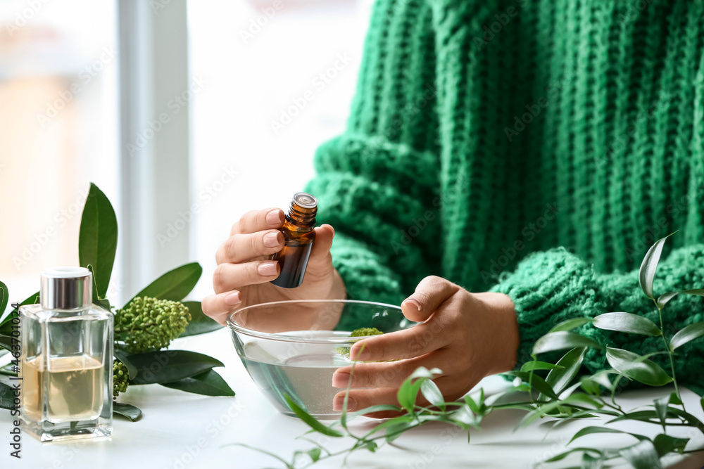 Woman adding essential oil to water in bowl on table