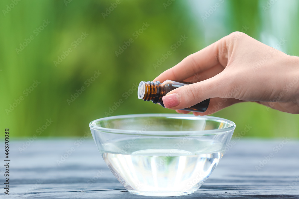 Woman adding essential oil to water in bowl on table