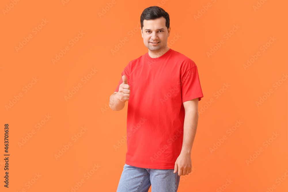 Handsome young man in stylish t-shirt showing thumb-up on color background