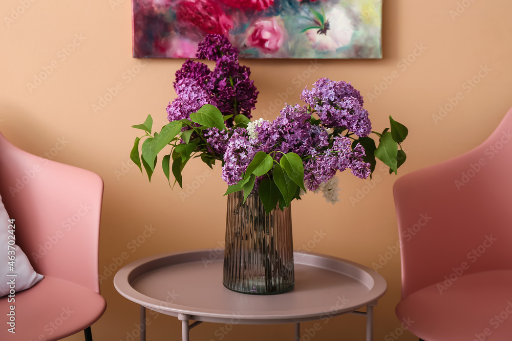 Glass vase with lilac flowers on table near color wall