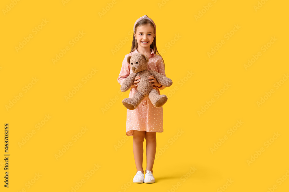 Cute little girl with teddy bear on yellow background