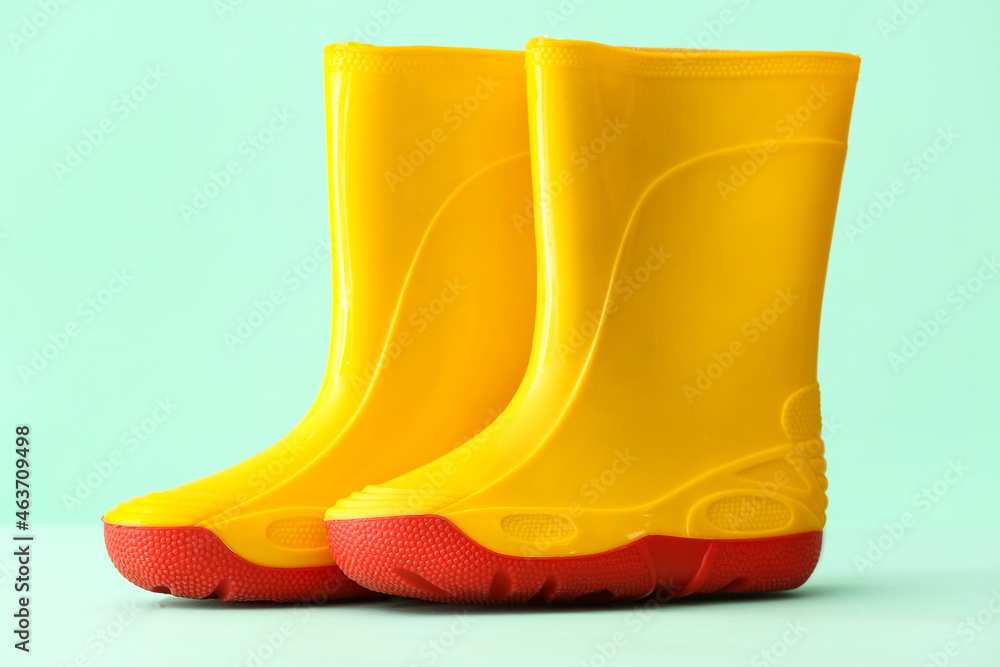 Pair of yellow rubber boots on color background