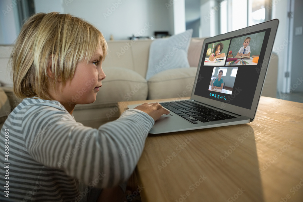 Caucasian boy using laptop for video call, with smiling diverse elementary school pupils on screen