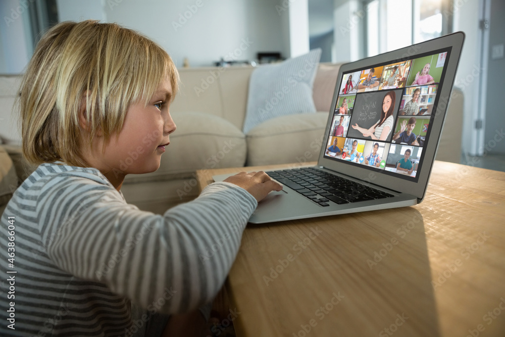 Caucasian boy using laptop for video call, with smiling diverse elementary school pupils on screen