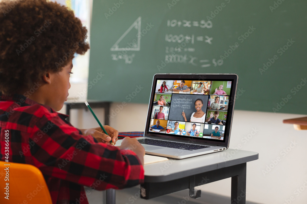 African american boy using laptop for video call, with diverse elementary school pupils on screen