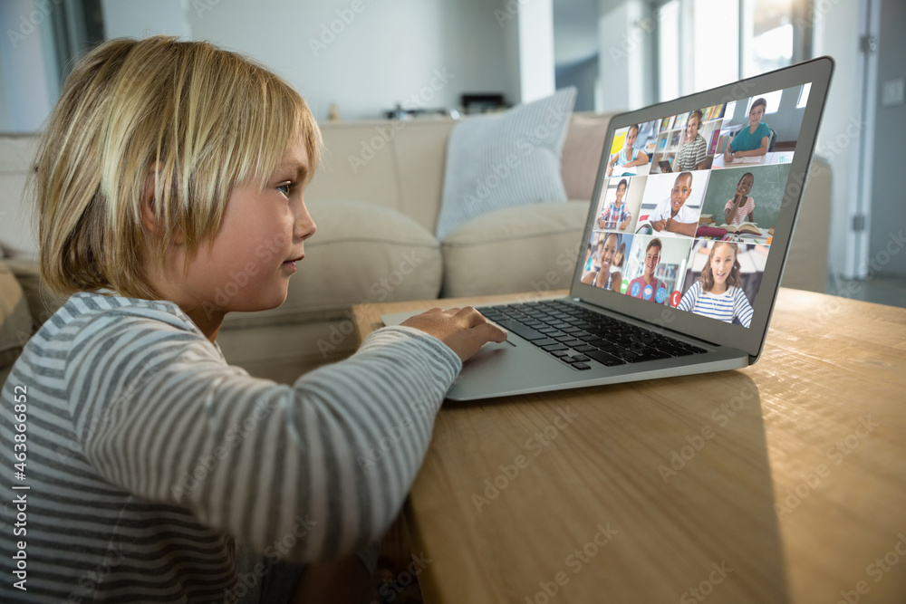 Caucasian boy using laptop for video call, with smiling diverse elementary school pupils on screen