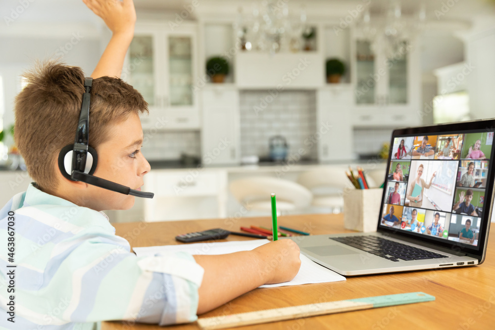 Caucasian boy raising hand for video call, with smiling diverse elementary school pupils on screen