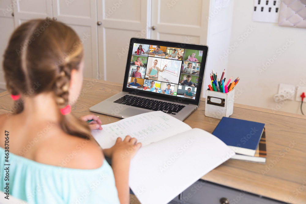 Caucasian girl using laptop for video call, with smiling diverse elementary school pupils on screen