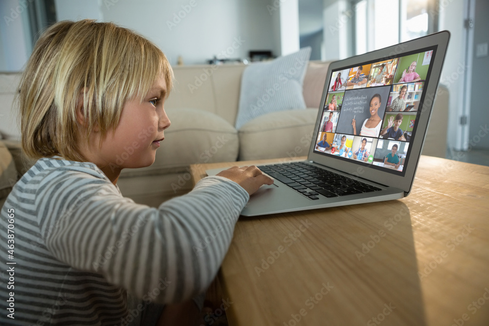 Caucasian boy using laptop for video call, with smiling diverse elementary school pupils on screen