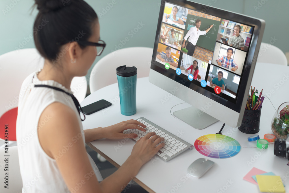 Asian girl using computer for video call, with smiling diverse elementary school pupils on screen