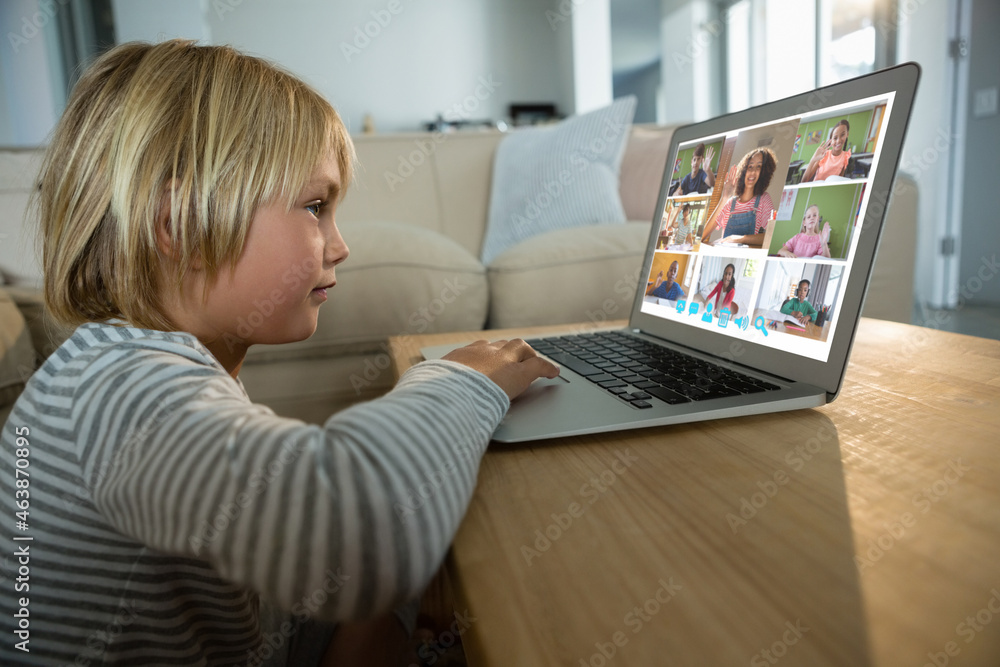 Smiling caucasian boy using laptop for video call, with diverse elementary school pupils on screen