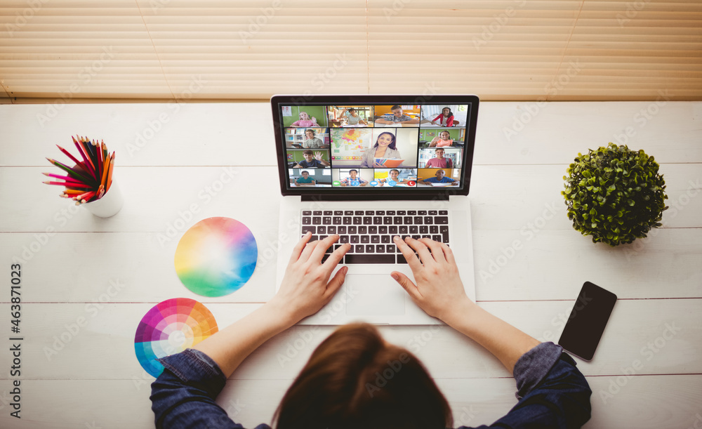 Caucasian woman using laptop for video call, with diverse elementary school pupils on screen