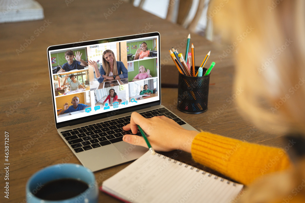 Caucasian woman using laptop for video call, with diverse elementary school pupils on screen