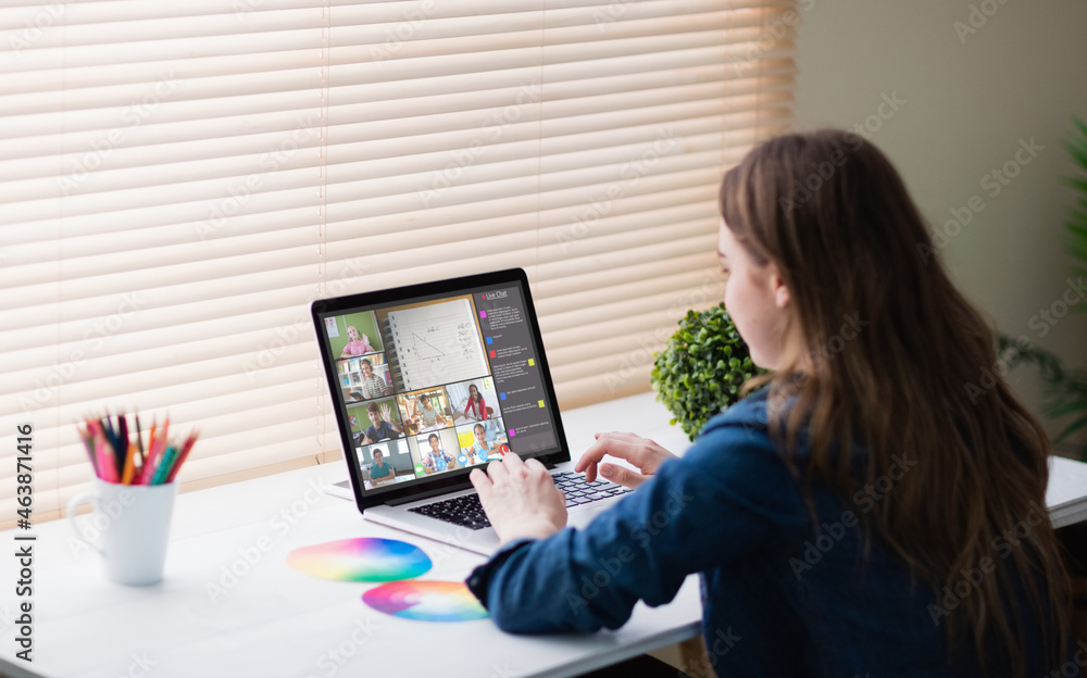 Caucasian woman using laptop for video call, with smiling diverse elementary school pupils on screen