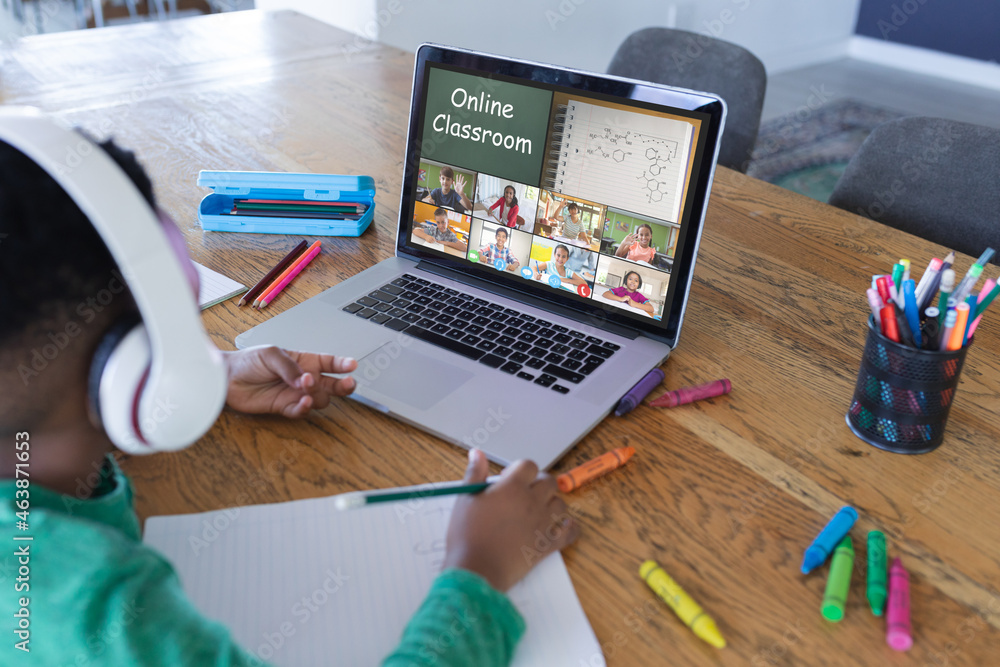 African american boy using laptop for video call, with elementary school pupils on screen