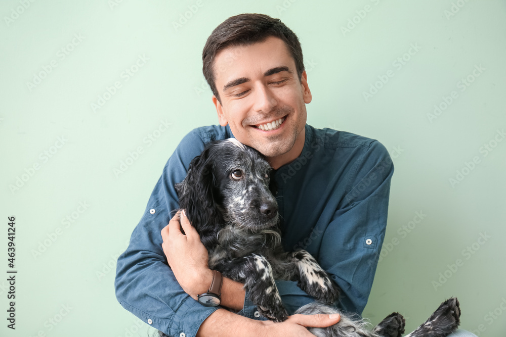 Happy young man with cute dog on color background