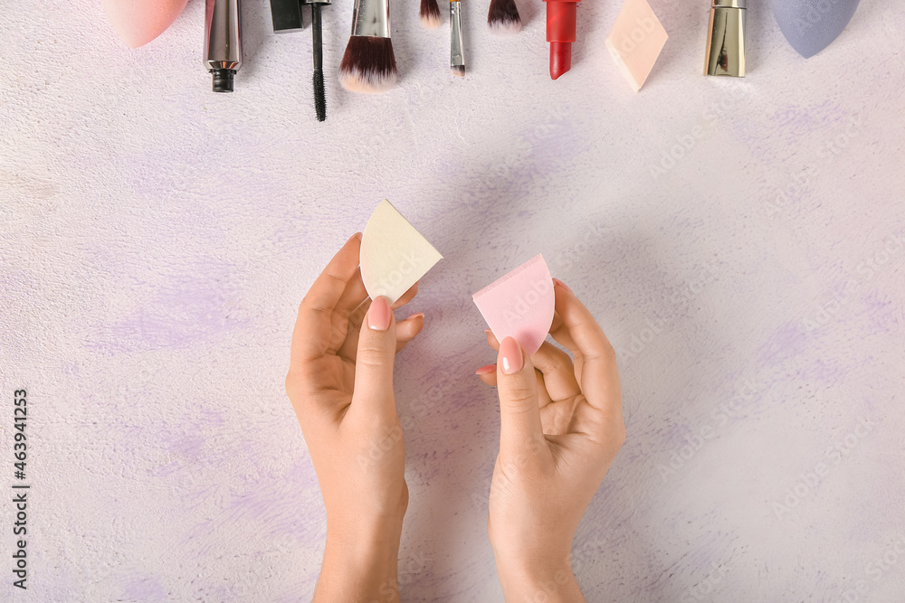 Female hands with stylish makeup sponges and decorative cosmetics on light background