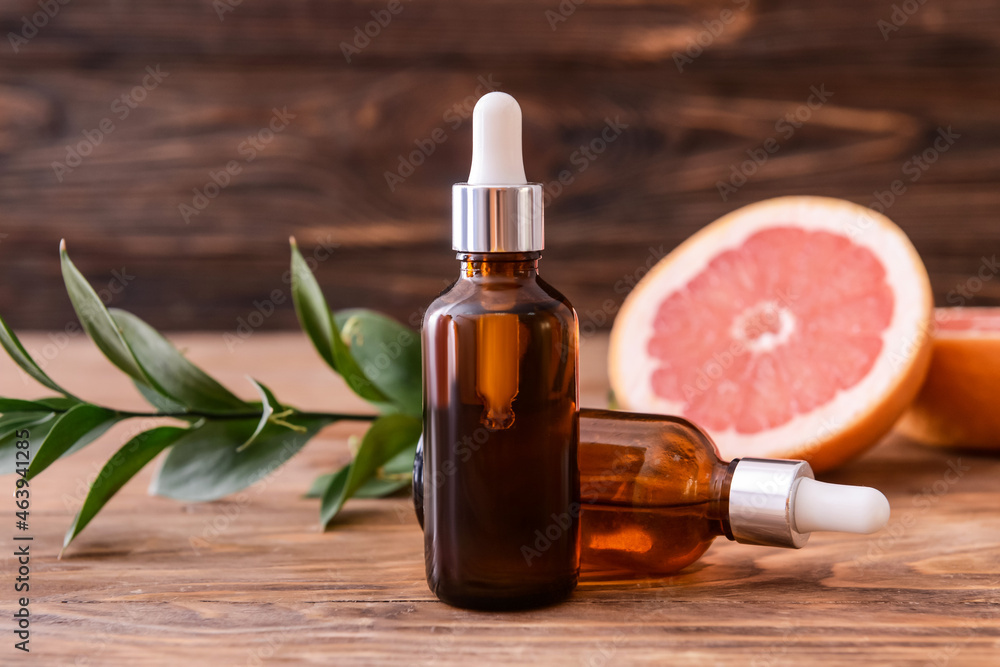 Bottles of grapefruit essential oil on wooden background