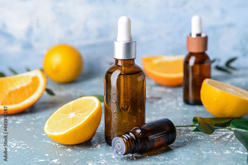 Bottles of citrus essential oils on color background