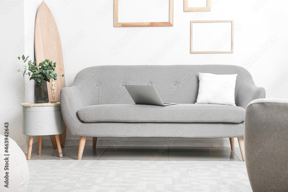 Grey modern sofa and glass vase with eucalyptus on table near light wall