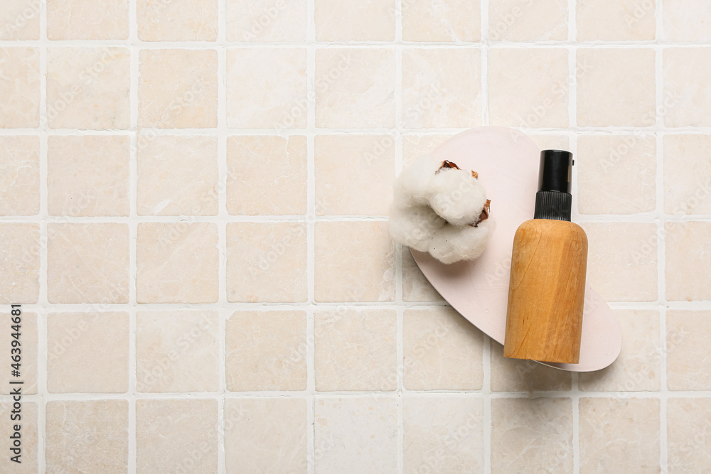 Bottle of cosmetic product and cotton flower on light tile