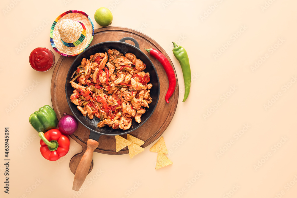 Frying pan with tasty Fajita, sauce and sombrero hat on color background