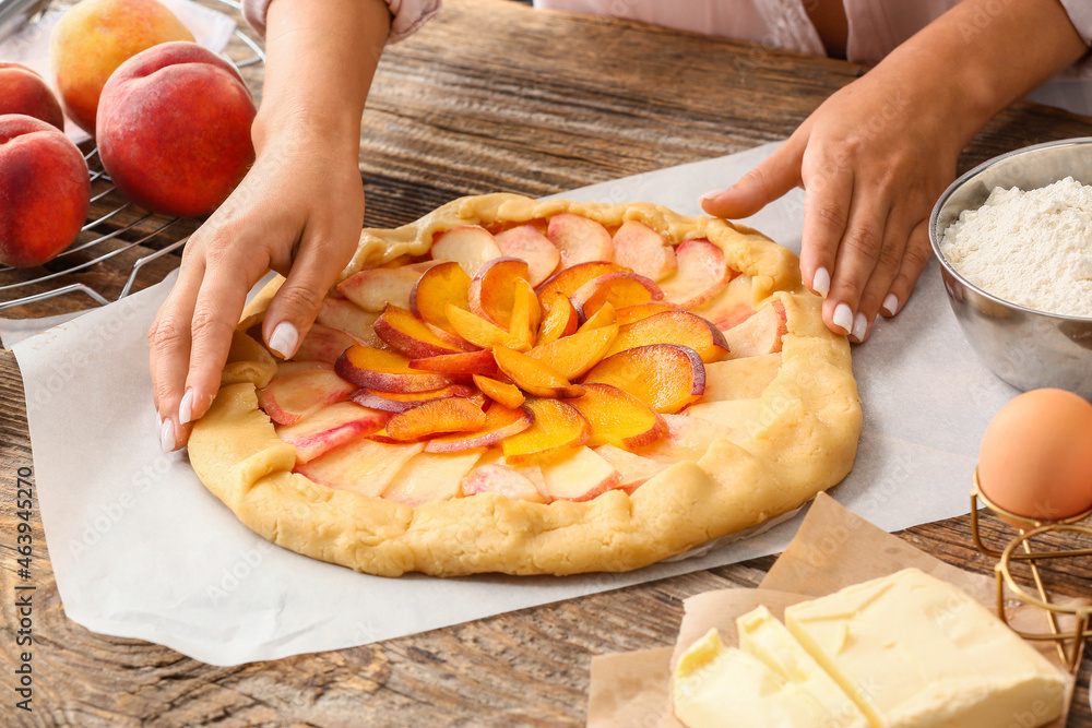 Woman preparing tasty peach galette at table