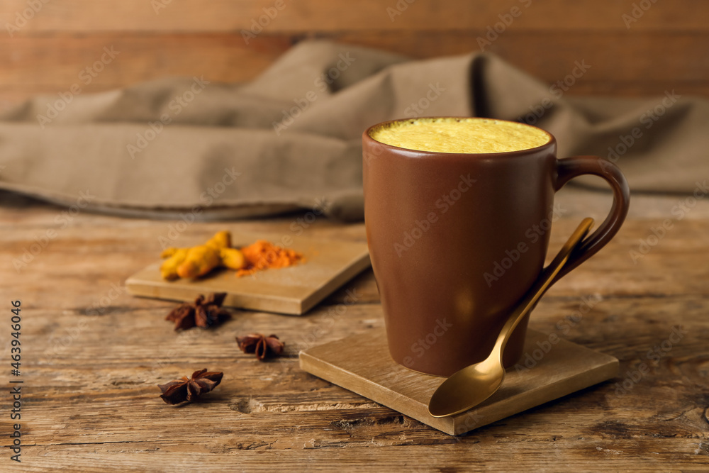 Cup of healthy turmeric latte with powder and star anise on wooden table