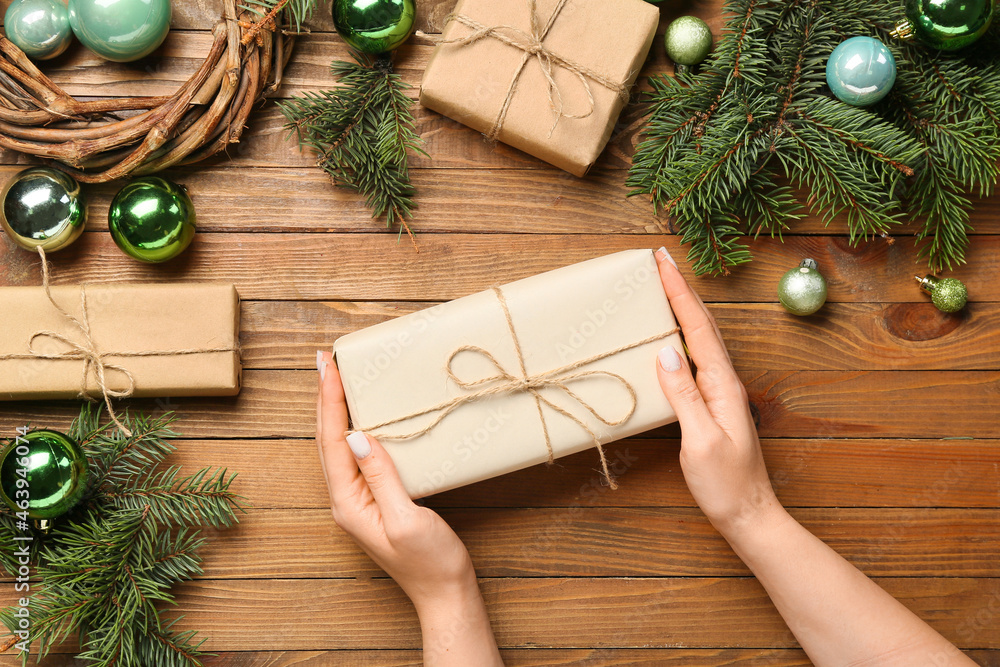 Female hands with gift boxes, fir branches and Christmas balls on wooden background, closeup