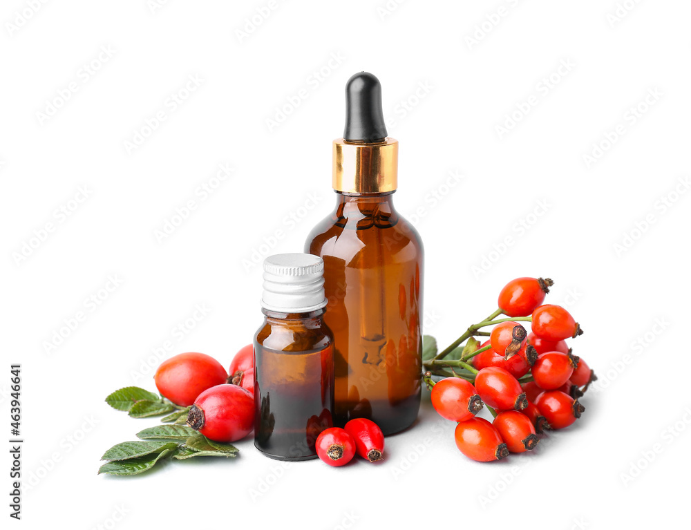 Bottles of essential oil and rose hip berries on white background