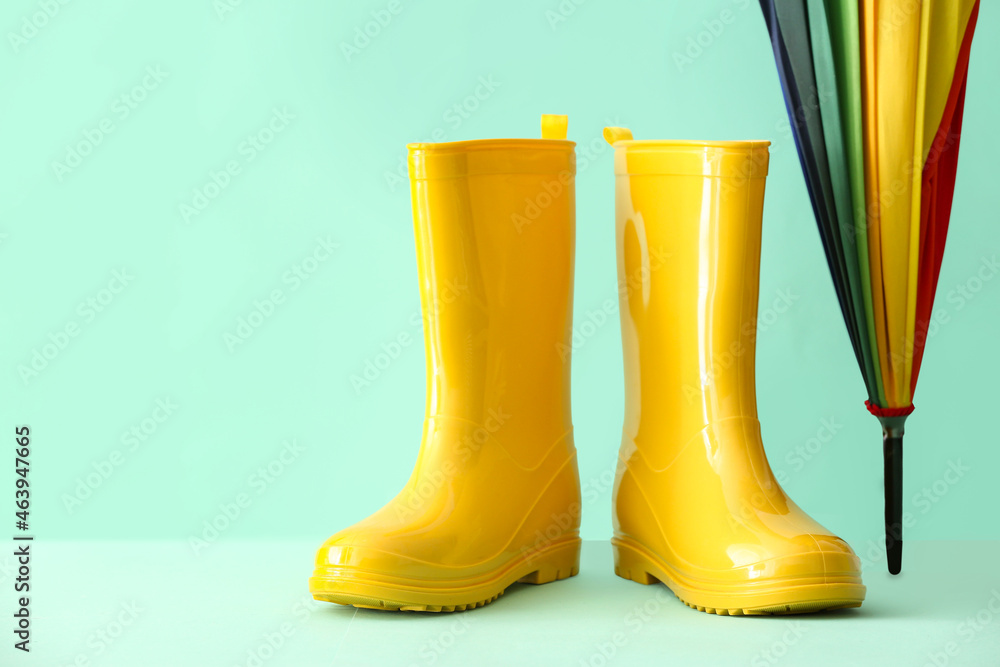 Rubber boots and umbrella on color background, closeup