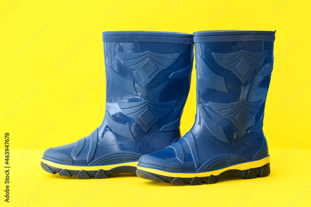 Pair of blue rubber boots on yellow background