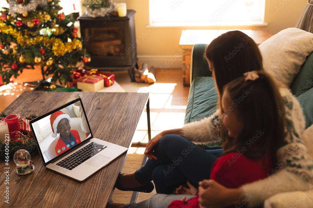 Caucasian mother and daughter in santa hats on christmas laptop video call with female friend