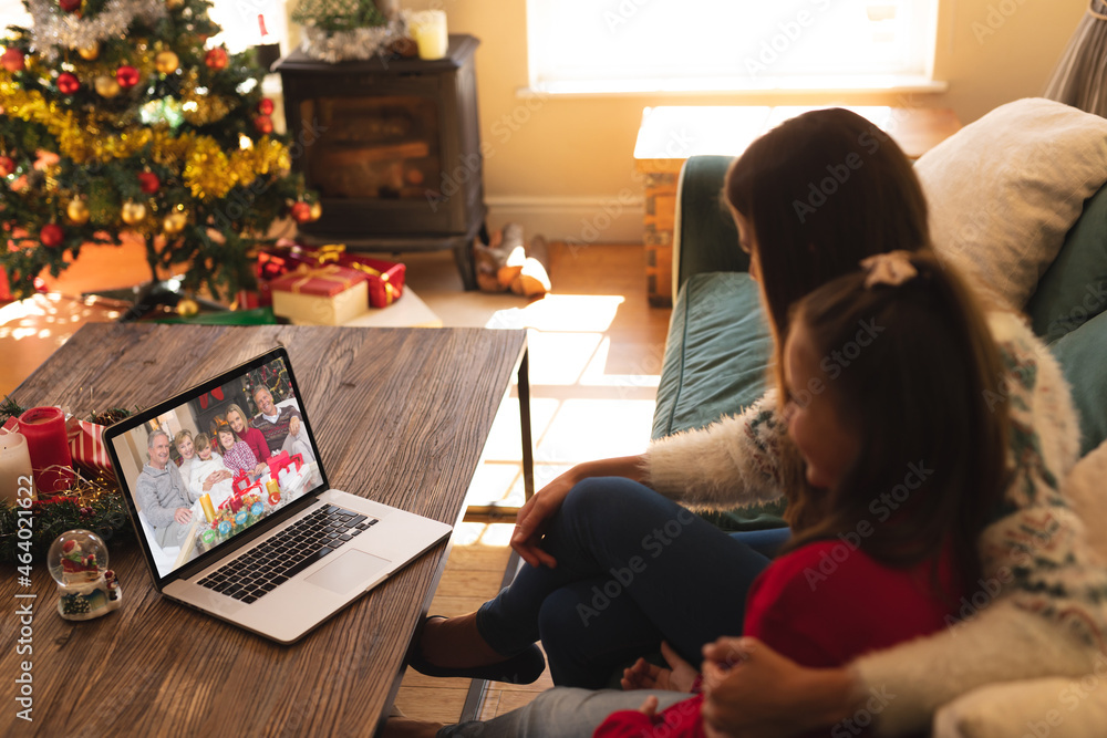 Caucasian mother and daughter in santa hat on christmas laptop video call with family