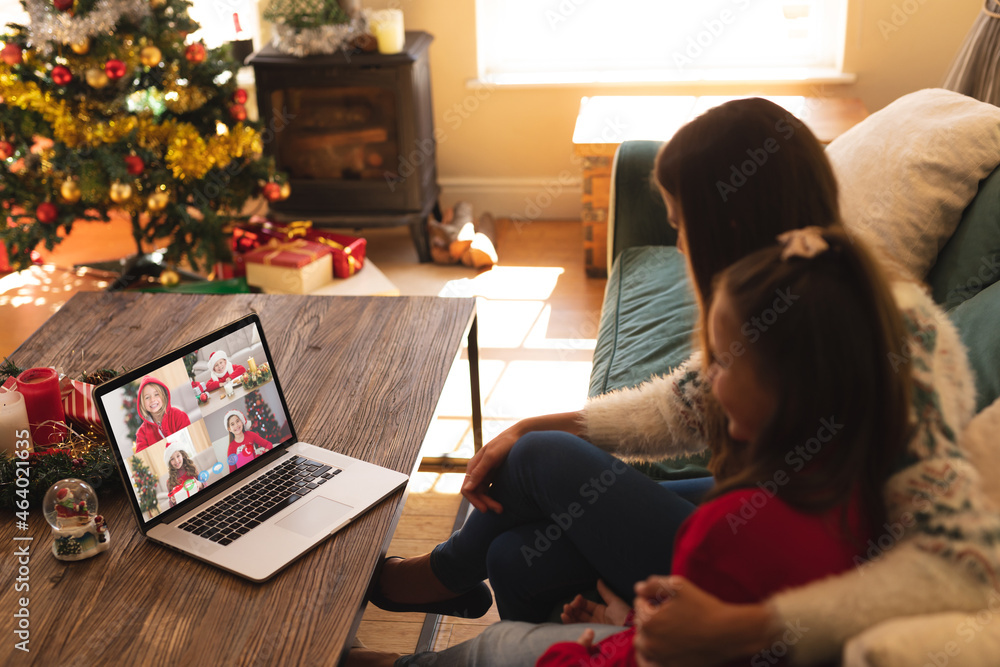 Caucasian mother and daughter in santa hat on christmas laptop video call with friends