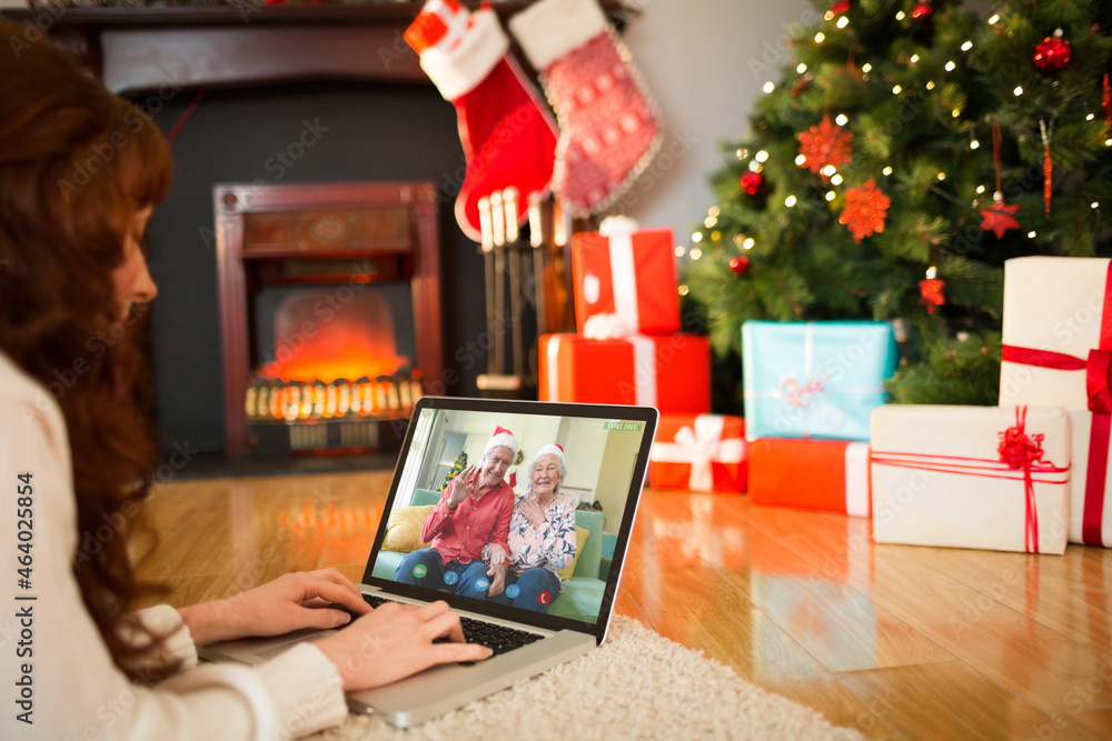 Caucasian woman on laptop christmas video call with smiling friends in santa hats