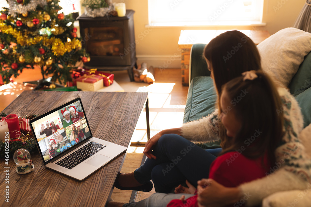 Caucasian mother and daughter on laptop christmas video call with smiling friends