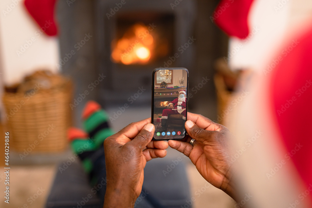 African american man in santa hat on christmas video call on smartphone with santa claus