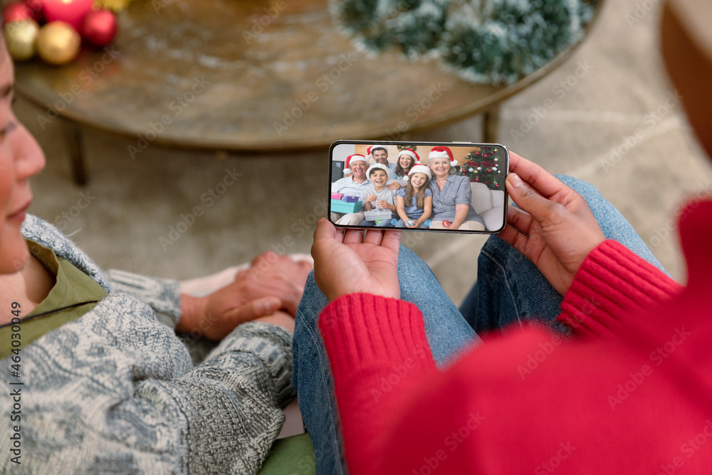 Two diverse female friends on christmas video call on smartphone with family