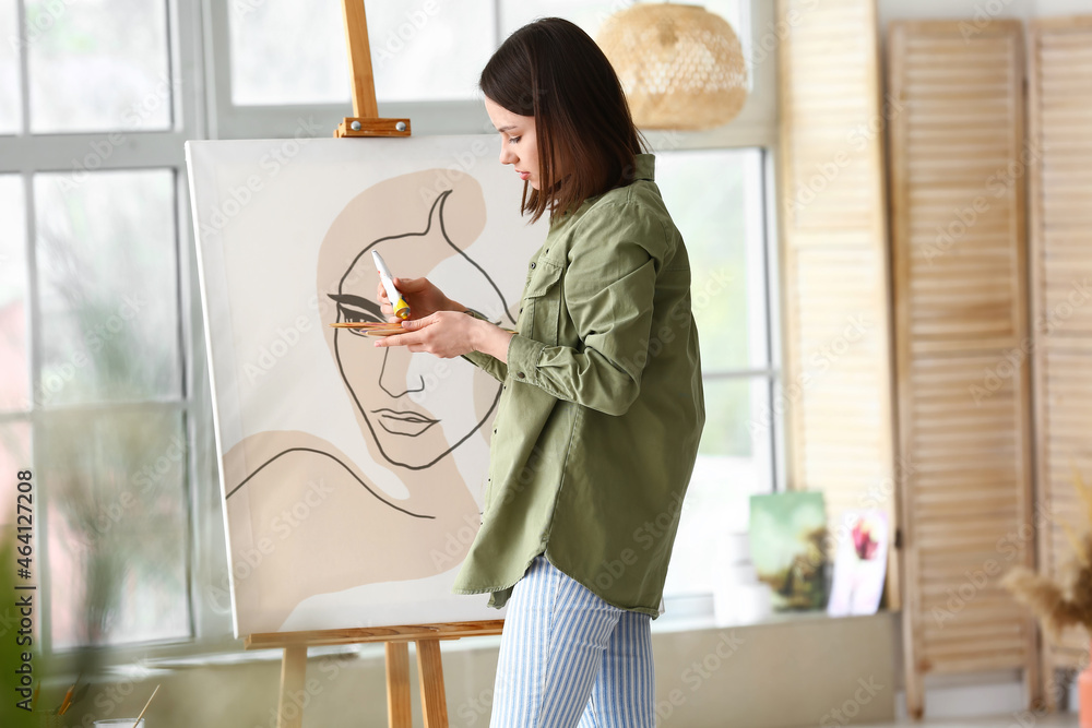 Young female artist painting in workshop