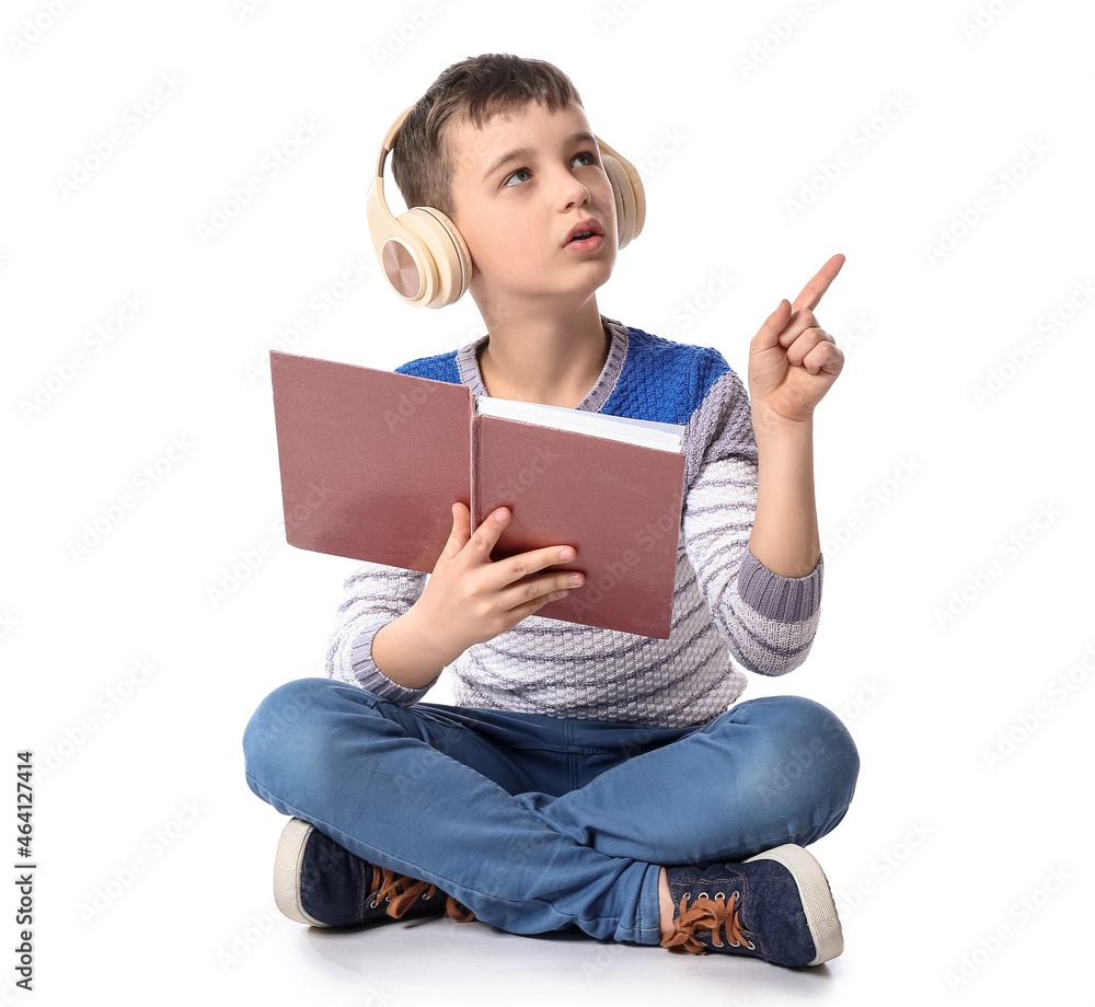 Little boy with book and headphones pointing at something on white background