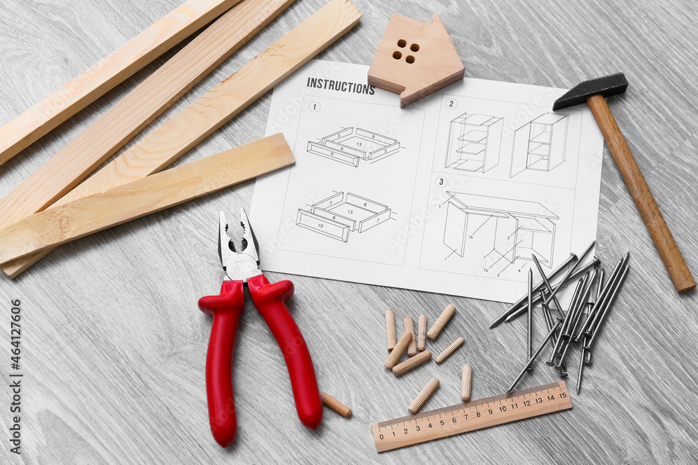 Furniture assembling instructions, wooden house and different tools on grey wooden background