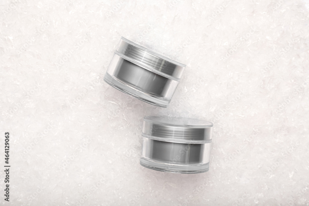 Silver jars of cosmetic product on light textured background