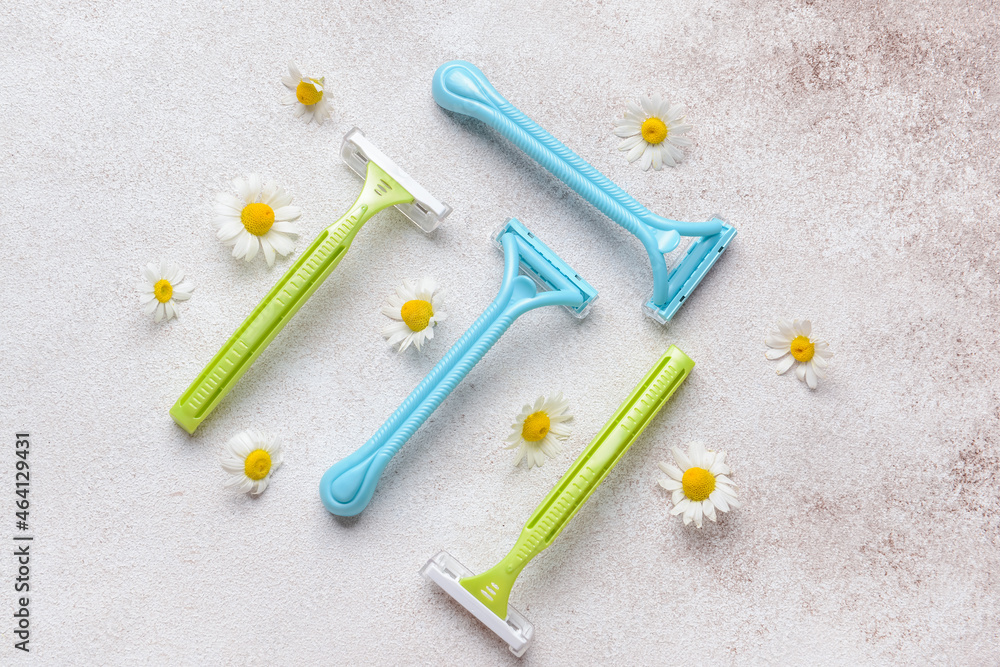 Safety razors and chamomile flowers on light background