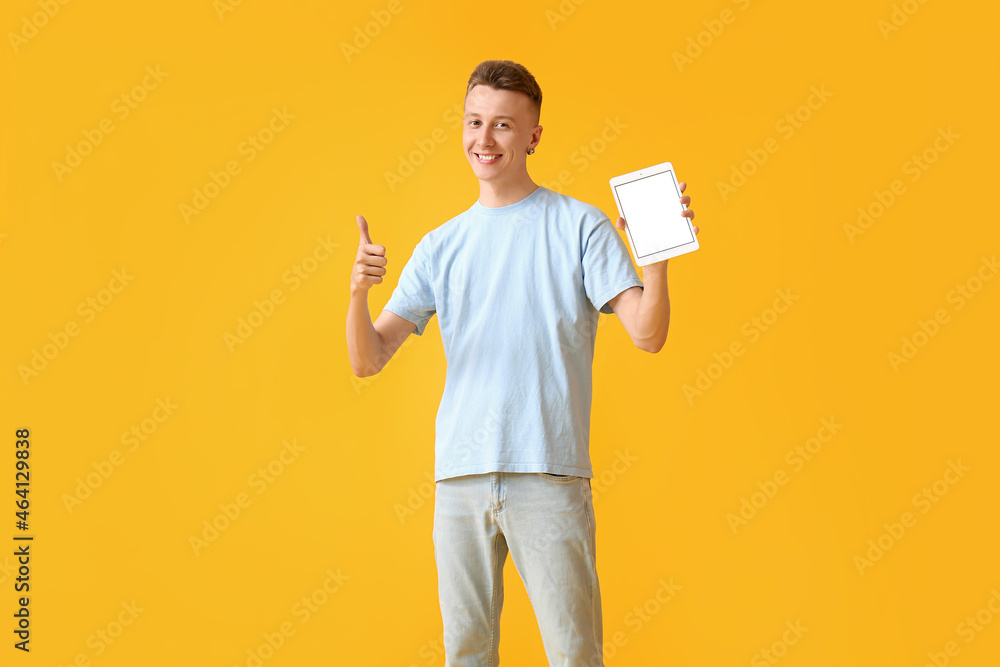 Young man with modern tablet computer showing thumb-up on yellow background