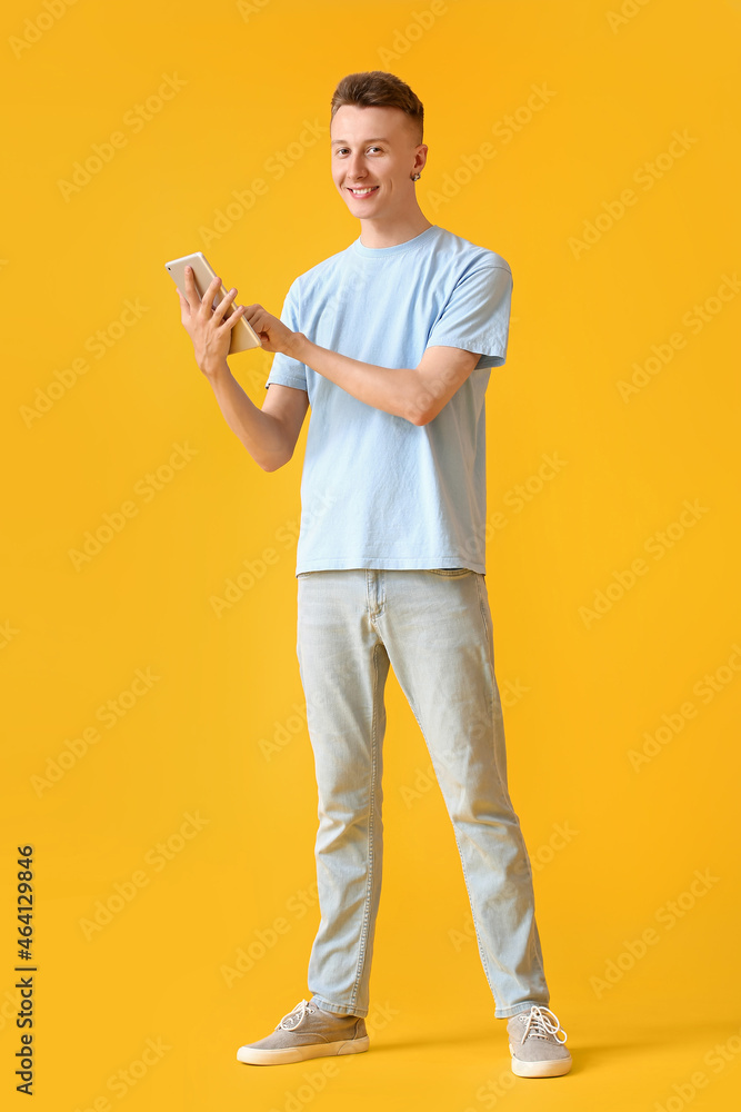 Young man using modern tablet computer on yellow background